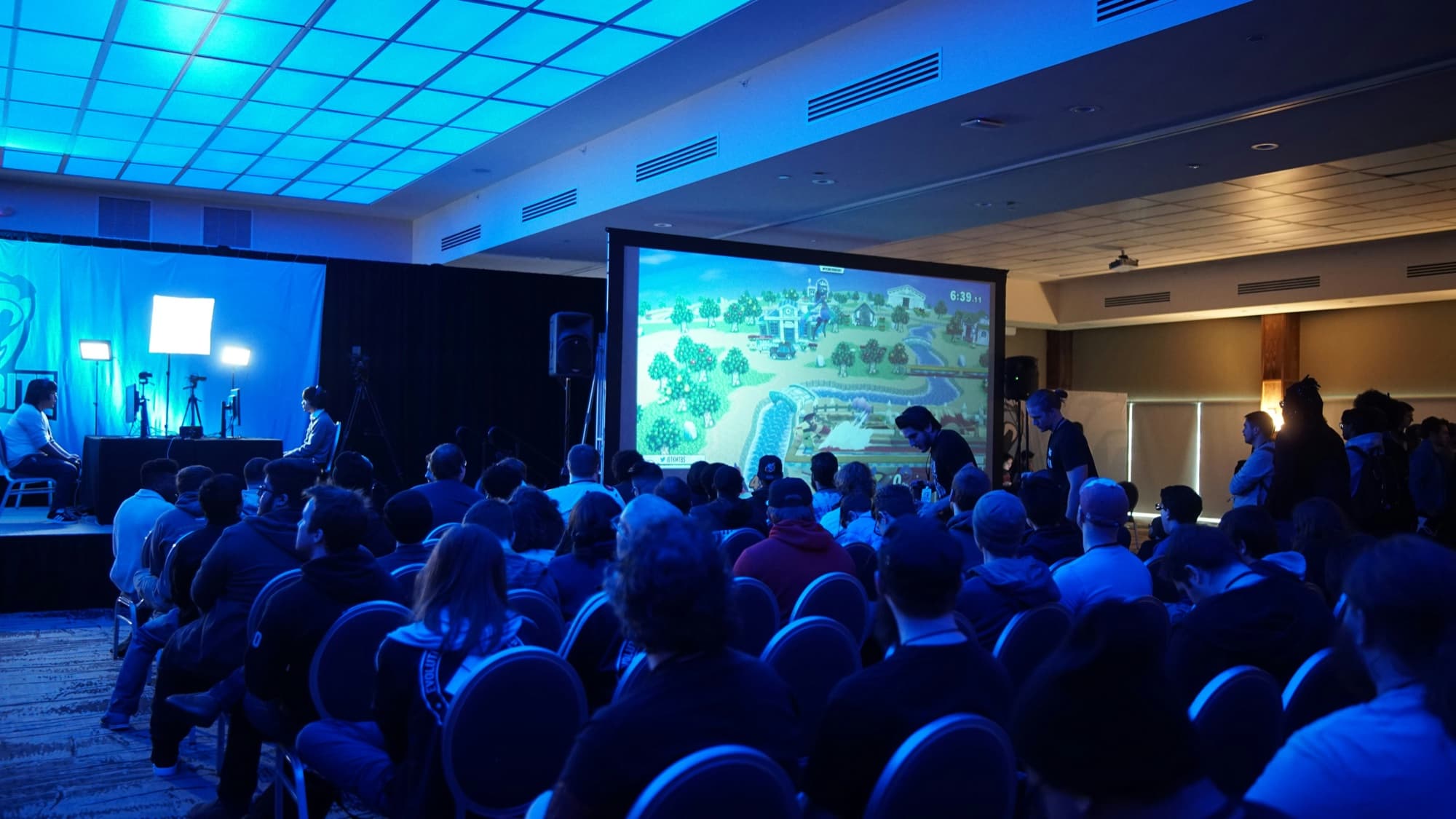 A packed conference audience seated in front of a bright screen