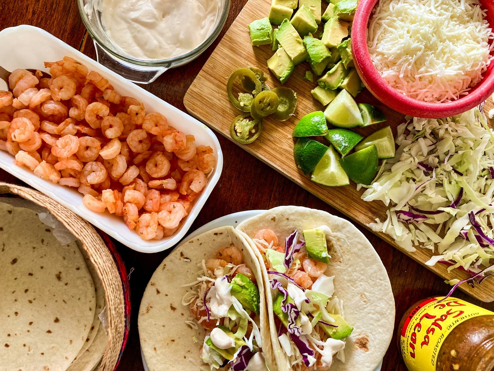 A table set for shrimp tacos with avocado, lime, and salsa